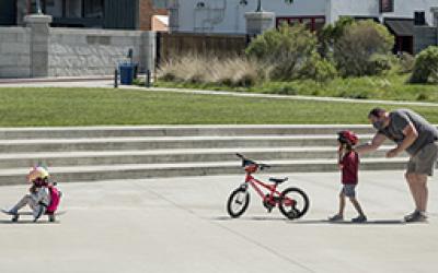 An adult teaches children how to ride a bike and a skateboard.