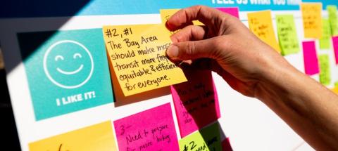 A hand places a Post-it note with comments on a display board at the Excelsior Sunday Streets event.