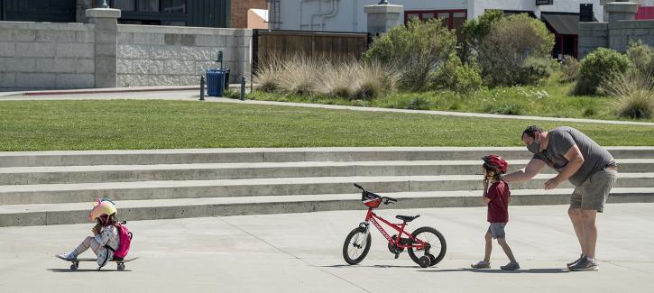 An adult teaching young children how to ride a bike and a skateboard.